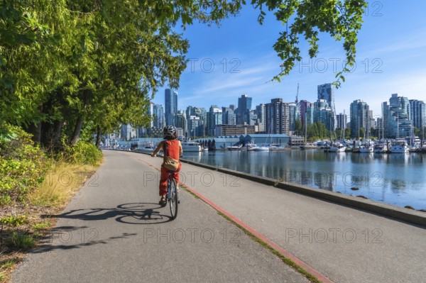 Tourist riding bicycle on the seawall in stanley park enjoying the scenic view of the vancouver skyline, british columbia, canada, on a sunny summer day