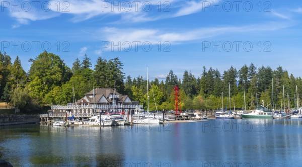 Panoramic view of the stanley park seawall with moored sailboats and yachts in coal harbour, featuring siwash rock and brockton point lighthouse on a sunny summer day