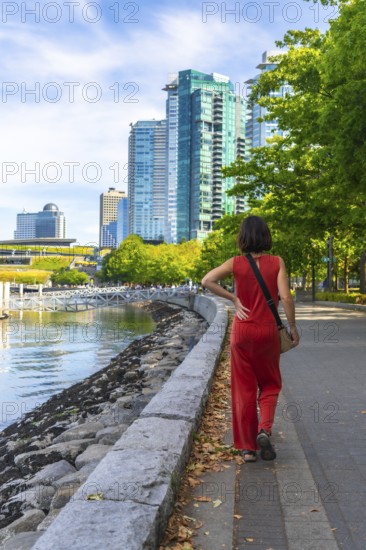Tourist walking on the seawall in vancouver downtown with modern buildings and green trees in the background, enjoying a sunny summer day in british columbia, canada