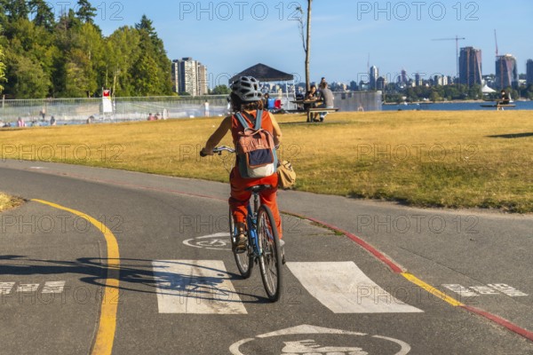 Tourist enjoying cycling in kitsilano beach park with english bay and the city of vancouver skyline in the background, during a sunny summer day in british columbia, canada