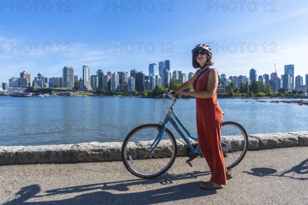 Young woman wearing a helmet stands next to her bicycle, enjoying a scenic waterfront view of vancouver's skyline in british columbia, promoting sustainable urban exploration