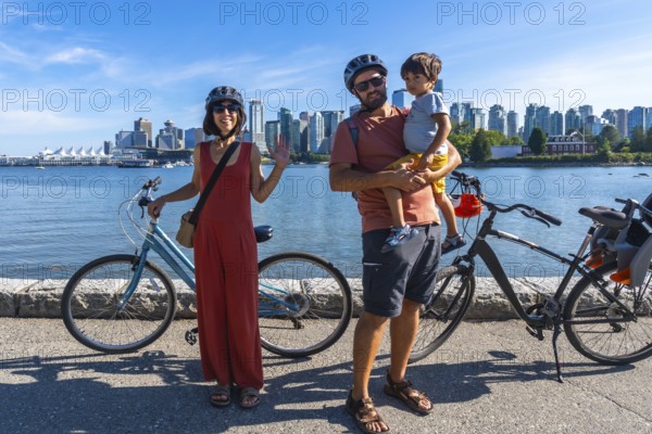 Happy family with bicycles enjoying a sunny day by the sea, taking a break from their ride with the cityscape of vancouver, british columbia, as a backdrop