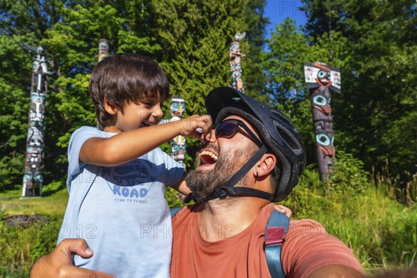 Playful father and son are enjoying a sunny day at brockton point in stanley park, vancouver, british columbia, surrounded by the iconic totem poles and lush greenery, creating a cherished memory