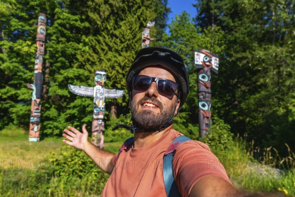 Cyclist wearing a helmet and sunglasses takes a selfie with totem poles at brockton point in stanley park. Vancouver. British columbia. Enjoying the cultural heritage and natural beauty of the city