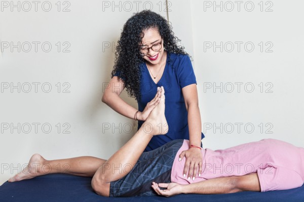 Smiling physiotherapist giving massage to lying patient. Female physiotherapist practicing lumbar rehabilitation physiotherapy, Lumbar physiotherapy treatment to a patient