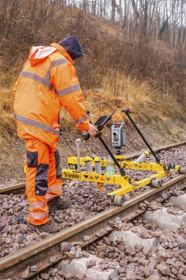Construction worker with measuring device device works on yellow equipment on rails in winter, tamping machine on Hermann, Hesse, Bahn, Althengstett, Calw district, Germany