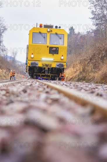 Yellow train on dirt road through forest with workers in the background, stuffing machine on Hermann, Hesse, railway, Althengstett, Calw district, Germany
