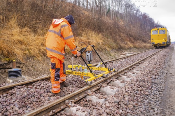 A worker operates a yellow device on the railroad tracks in an autumn landscape, stuffing machine on Hermann, Hesse, Bahn, Althengstett, Calw district, Germany