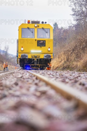 Yellow vehicle on gravel with construction workers in the forest, tamping machine on Hermann, Hesse, railway, Althengstett, Calw district, Germany