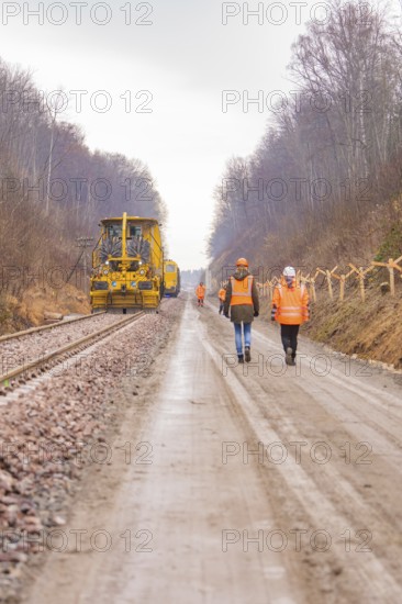 Construction worker on a rail line in the forest, accompanied by a yellow machine, tamping machine on Hermann, Hesse, railway, Althengstett, Calw district, Germany