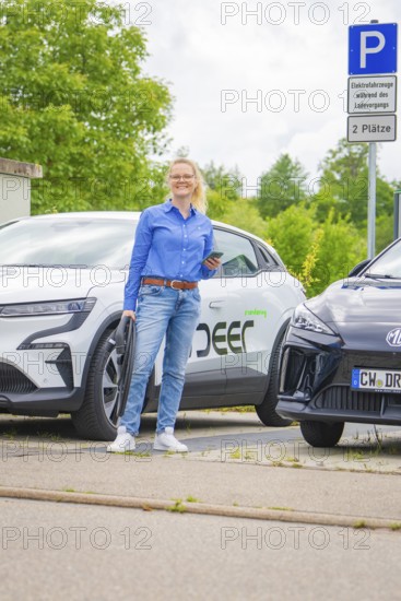 Woman standing in front of two electric cars in a parking lot with technological flair, Deer E-Carsharing, Calw, Germany