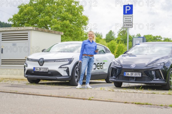 Two electric cars park side by side at a charging station, surrounded by green countryside, Deer E-Carsharing, Calw, Germany