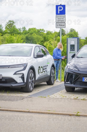 Woman at a charging station between two electric cars in a green parking lot, Deer E-Carsharing, Calw, Germany