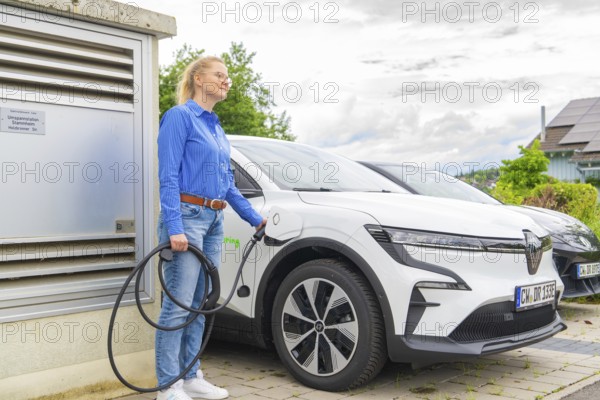 Woman wearing a blue shirt charges a white electric car at a charging station, Deer E-Carsharing, Calw, Germany