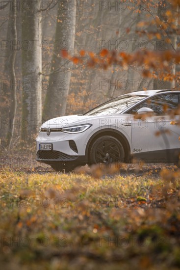 A white car drives on a forest path surrounded by autumn trees, Deer E-Carsharing, VW ID4, Calw, Germany