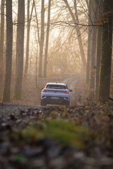 A car drives at sunrise on a forest path surrounded by trees, Deer E-Carsharing, VW ID4, Calw, Germany