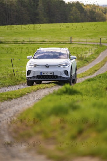 White car driving on a dirt road through green meadow landscape in daylight, Deer E-Carsharing, VW ID4, Calw, Germany