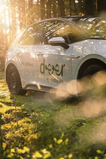A car in the forest, illuminated by sunbeams, promotes a car sharing offer, Deer E-Carsharing, VW ID3, Calw, Germany