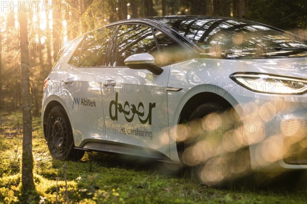 A car is parked in the forest, illuminated by sunbeams, part of a car sharing service, Deer E- Carsharing, VW ID3, Calw, Germany
