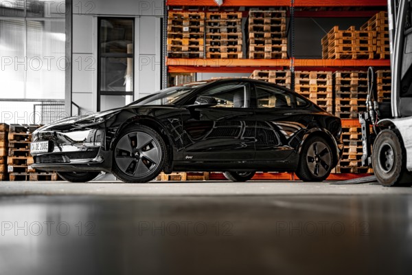 Black car in a warehouse next to wooden pallets and machines, Deer e-Carsharing, Tesla Model 3, Calw, Germany