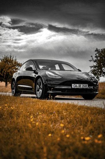 Black car on country road with orange fields under dramatic sky, Deer E- car sharing, Tesla Model 3, Calw, Germany