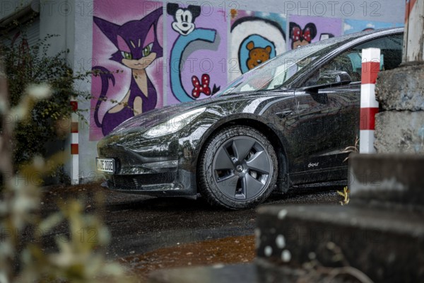 Black car in an urban environment with colorful graffiti wall and wet road, Deer e-Carsharing, Tesla Model 3, Calw, Germany