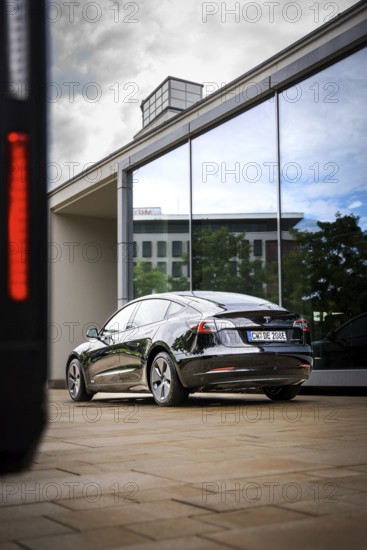 Black car in front of a modern glass façade reflecting the sky, Deer E-Carsharing, Tesla Model 3, Calw, Germany
