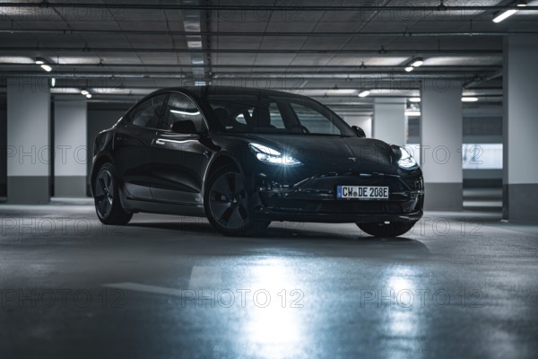 Black car parked in an urban underground car park surrounded by cool artificial light and shade, Deer E-Carsharing, Tesla Model 3, Calw, Germany