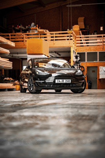 Black car in an industrial-looking workshop with wooden details, parked on concrete floor, deer e-car sharing, Tesla Model 3, Calw, Germany