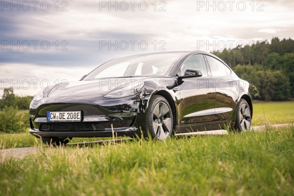 Black car on a country road surrounded by green fields under cloudy sky, Deer E-Carsharing, Tesla Model 3, Calw, Germany