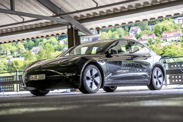 Black car in a bright, covered parking garage with views of green hills, Deer E-Carsharing, Tesla Model 3, Calw, Germany