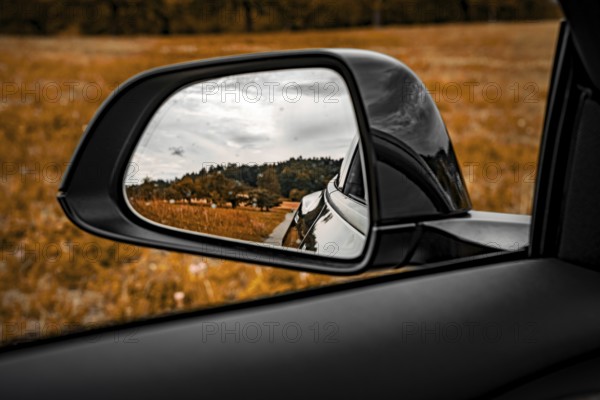View through the side mirror of a car of a rural landscape with meadow and trees, Deer E-Carsharing, Tesla Model 3, Calw, Germany