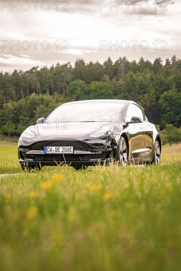 Black car on a country road with a view of green fields and forest, Deer E-Carsharing, Tesla Model 3, Calw, Germany