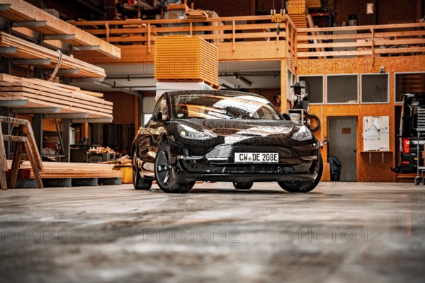 Black car parked in a workshop with wooden shelves and industrial atmosphere, Deer E-Carsharing, Tesla Model 3, Calw, Germany