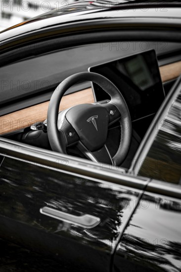 Black steering wheel with wood decor in modern car interior, side perspective, Deer e-car sharing, Tesla Model 3, Calw, Germany