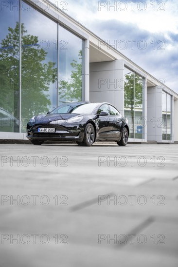 Black Tesla in front of a reflecting glass building on a cloudy day, Deer E-Carsharing, Tesla Model 3, Calw, Germany