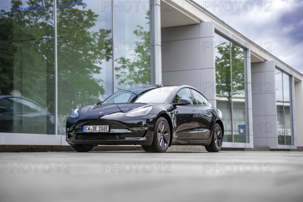 Black Tesla in front of a glass building with trees in the background, Deer e-Carsharing, Tesla Model 3, Calw, Germany
