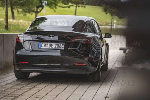 Black car from behind on a road with green landscape in the background, Deer e-Carsharing, Tesla Model 3, Calw, Germany