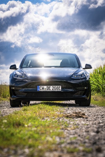 Black car on rural road in sunny weather, surrounded by fields and clouds, Deer E-Carsharing, Tesla Model 3, Calw, Germany