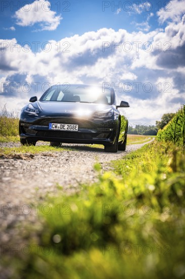 Black car driving on a dirt road through picturesque landscape under blue sky, Deer E-Carsharing, Tesla Model 3, Calw, Germany