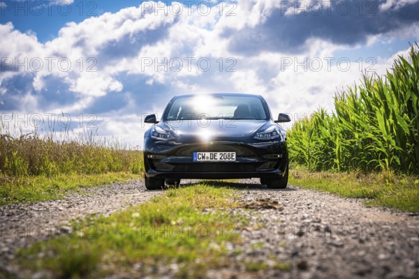 Front view of black car on rural road with cloudy sky, Deer E-Carsharing, Tesla Model 3, Calw, Germany