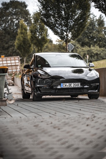 Black car from the front with surroundings and trees in the background, Deer e-Carsharing, Tesla Model 3, Calw, Germany