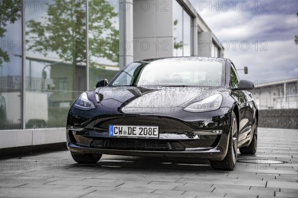 Wet Tesla in front of a modern glass building, covered with raindrops, Deer E-Carsharing, Tesla Model 3, Calw, Germany