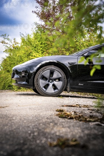 Side close-up of a black car on an asphalt road surrounded by plants, Deer E- car sharing, Tesla Model 3, Calw, Germany