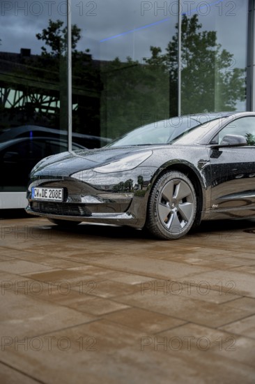 Black car in front of a glass building on rain-wet ground, Deer E-Carsharing, Tesla Model 3, Calw, Germany