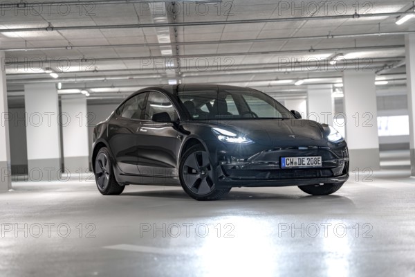Black Tesla, headlights on, placed centrally in empty parking garage, Deer e-Carsharing, Tesla Model 3, Calw, Germany