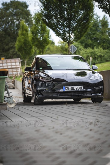 Black car from the front on a paved road with background landscape, Deer E-Carsharing, Tesla Model 3, Calw, Germany