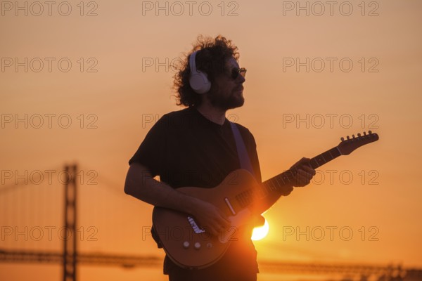 Hipster street musician in black playing electric guitar in street outdoors on sunset