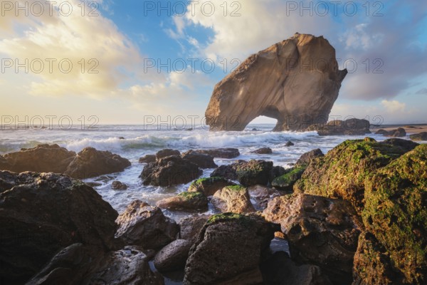 Penedo do Guincho stands majestically at Praia da Santa Cruz as ocean waves crash against the sandy beach during sunset