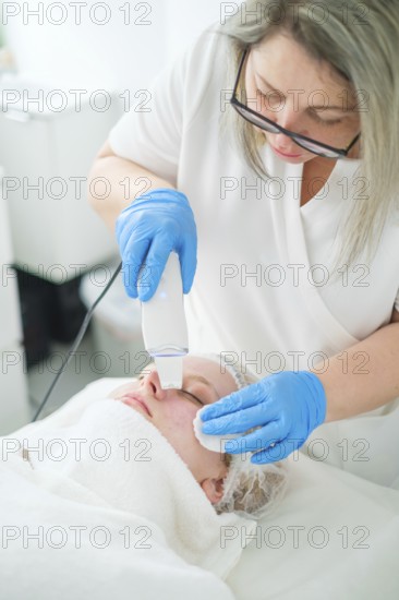 A pro esthetician cosmetologist uses a metal spatula for ultrasonic facial cleansing to exfoliate and refresh the client's skin